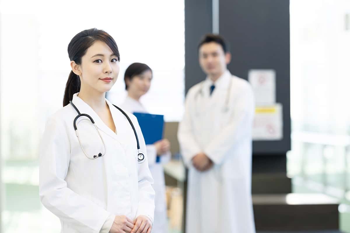 Woman in medical whites with a stethoscope around her neck looks into the image.